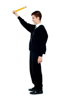 Side view portrait of school boy drawing imaginary diagram with big yellow pencil