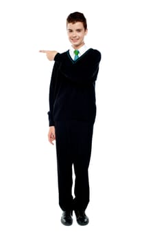 Full length portrait of attractive school boy pointing towards copy space area
