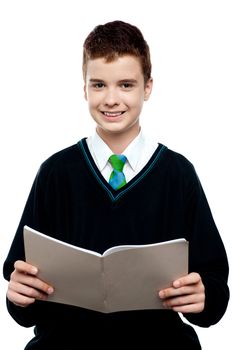 Charming schoolboy holding workbook and looking at camera