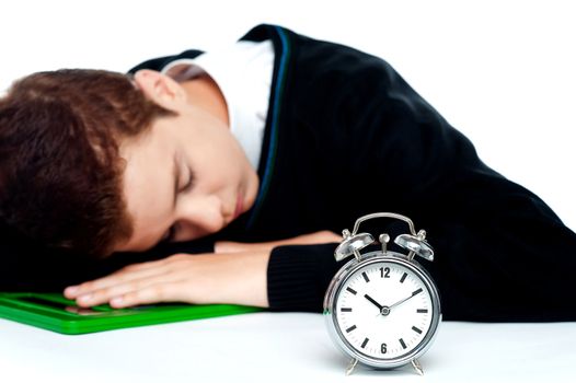 Tired schoolboy sleeping on calculator with alarm clock beside him