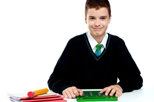 Smiling young boy using calculator sitting in classroom
