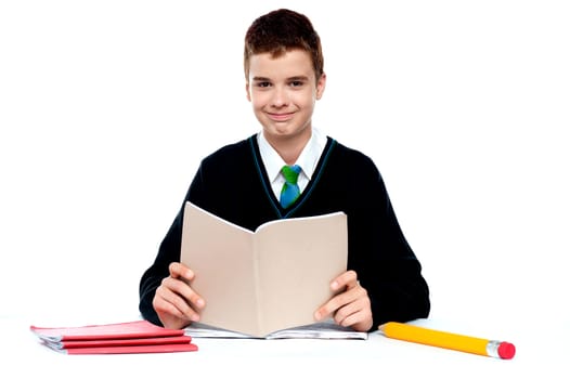 Cute school kid holding notebook and reading looking at camera
