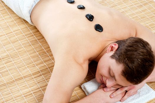Smiling young man lying on mattress with hot stones on his back