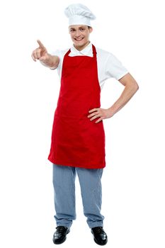Male chef in uniform pointing away and smiling against white background