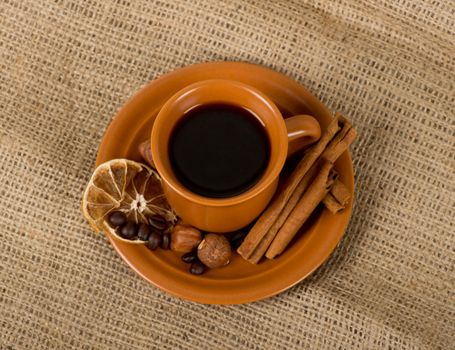 Closeup shot of freshly prepared cup of italian espresso with cinnamon, coffe beans, nuts and lemon over sacking
