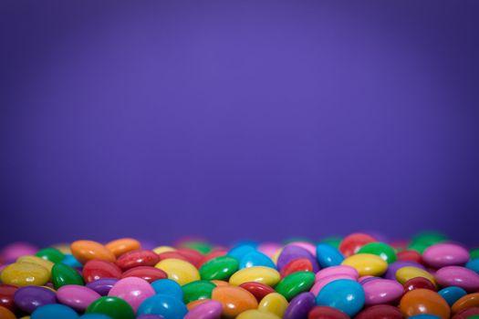 A bunch of chocolate buttons, in various colors such as pink, purple and yellow with a blue background.
