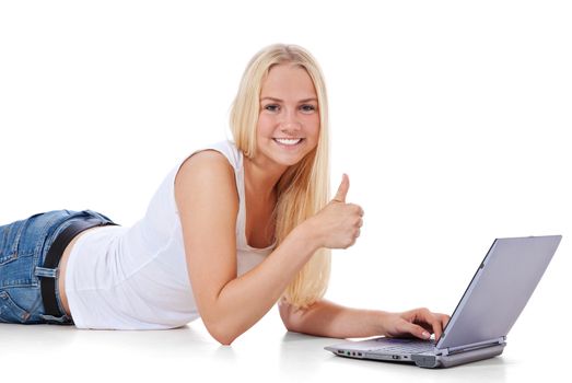 Attractive teenage girl lying on floor using laptop showing thumbs up. All on white background.