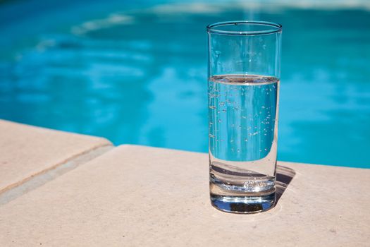 Glass of water standing near swimming pool.