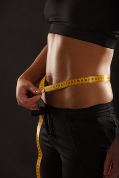 Photo of a tanned slim young woman measuring her waistline.
