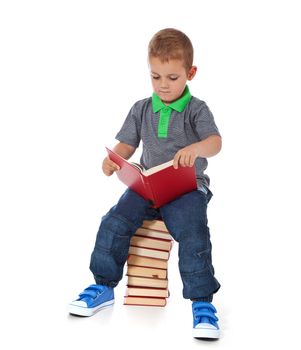 Full length shot of a cute little boy sitting on a pile of books, reading. All isolated on white background.
