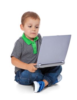 Full length shot of a cute little boy sitting on the floor with a computer. All isolated on white background.