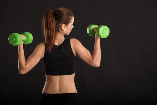 Photo of a toned young female exercising with dumbbells.