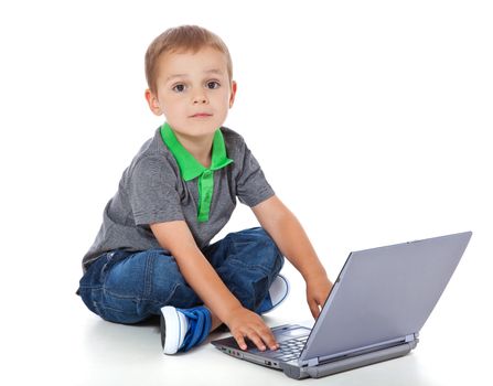 Full length shot of a cute little boy sitting on the floor with a computer. All isolated on white background.