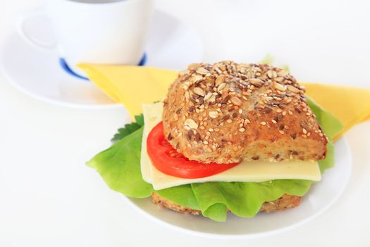 Roll with cheese and lettuce next to a cup of coffee.
