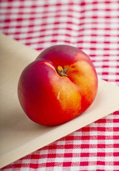 Single red peach over a wooden plate