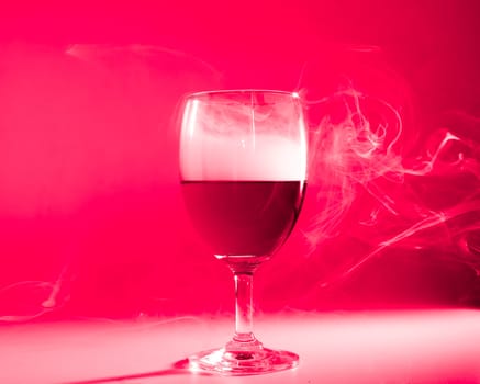 Glass of wine with smoke on red back ground and back light