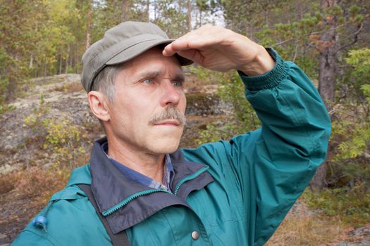 An elderly traveller looking into the distance in an autumn wood