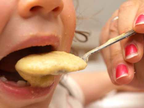 A toddler eating porridge, closeup, person with manicure