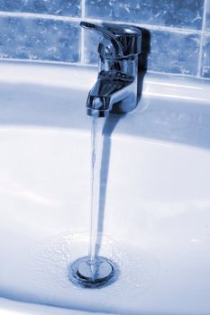 Water tap with a water stream. Blue tone image