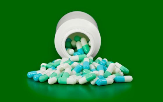 Open bottle medicine pill spilling out isolated on green background