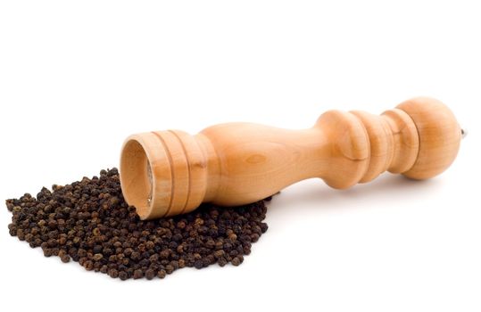 Wooden pepper mill lying on peppercorns, isolated on white background.