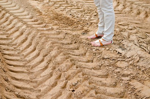 woman legs stand on quarry sand truck tracks.