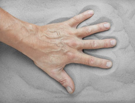 The hand of the old man in the grey sand
