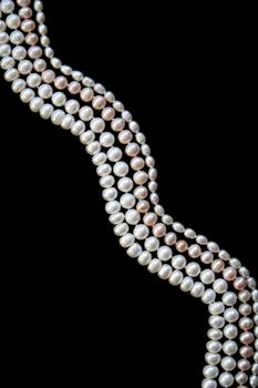 White and pink pearls on the black silk as background 