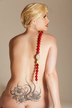 Naked woman from behind with a tattoo designer and chain
