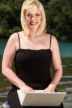 Young woman spends her free time with a laptop on the lake