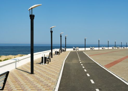 Deserted seafront promenade with a road surrounded by neat paving and a row of stylish modern streetlamps with benches to relax and enjoy the view over the ocean