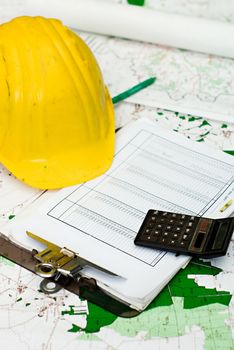 Objects representing the financial aspect of construction - a yellow hardhat, clipboard with a table of figures, a pen, and a calculator - all sitting on top of area plans.