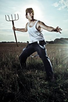 Young alerted farmer standing in field with pitchfork ready to fight