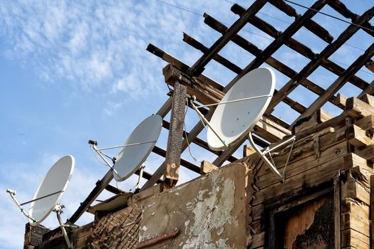Ruined building with stripped roof exposing the roofing timbers to the sky and a row of three satellite dishes on the exterior grungy wall