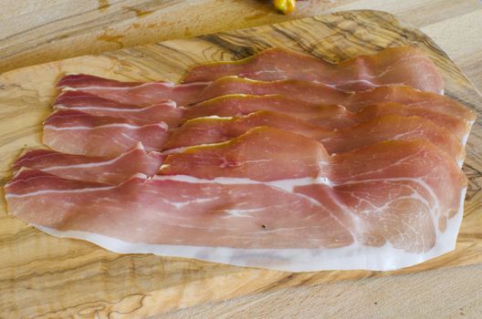 Some slices of Prosciutto Crudo on a wooden base