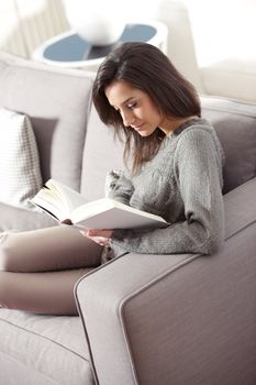 Portrait of a young woman lying on couch with book