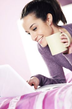 Happy casual  young lady using laptop while lying in bed