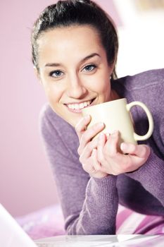 Portrait of a pretty happy young woman holding a cup of coffee in bed