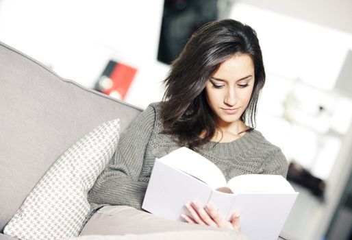 Portrait of a young woman lying on couch with book