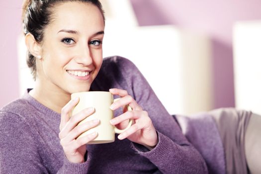 Portrait of a pretty happy young woman holding a cup of coffee in bed