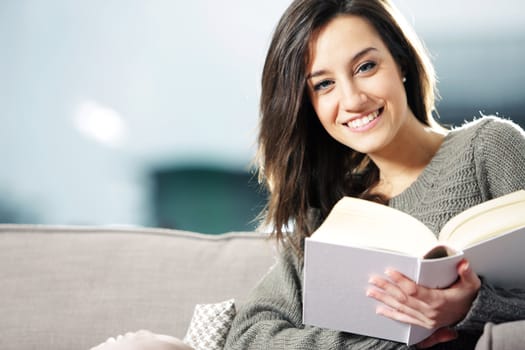 Portrait of a happy young woman lying on couch with book