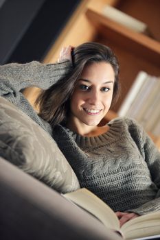 Portrait of a happy young woman lying on couch with book