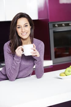 Beautiful young  woman having coffee while at the kitchen