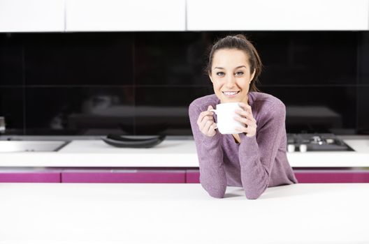 Beautiful young  woman having coffee while at the kitchen