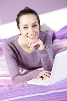 Portrait of a young female relaxing in bed while using laptop