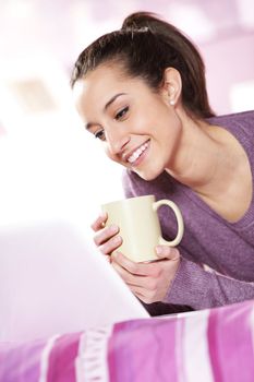 pretty girl smiles at the laptop with a cup of coffee in hand