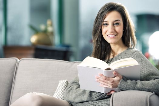 Portrait of a happy young woman lying on couch with book