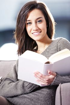Portrait of a happy young woman lying on couch with book