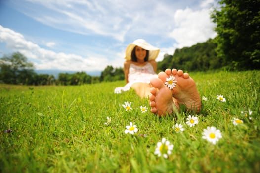 a smiling young woman is lying on a green lawn, with a daisy between her toes; shallow deep of field; selective focus; DOF