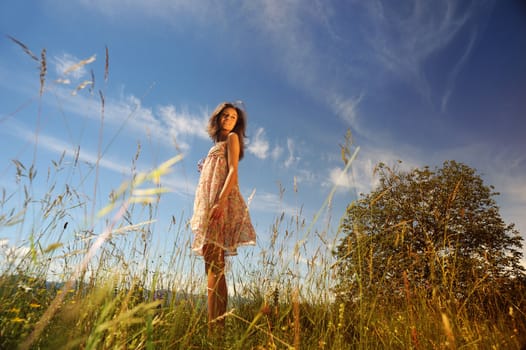 a young woman smiling in the midst of a green lawn, she looks at the sky, so carefree